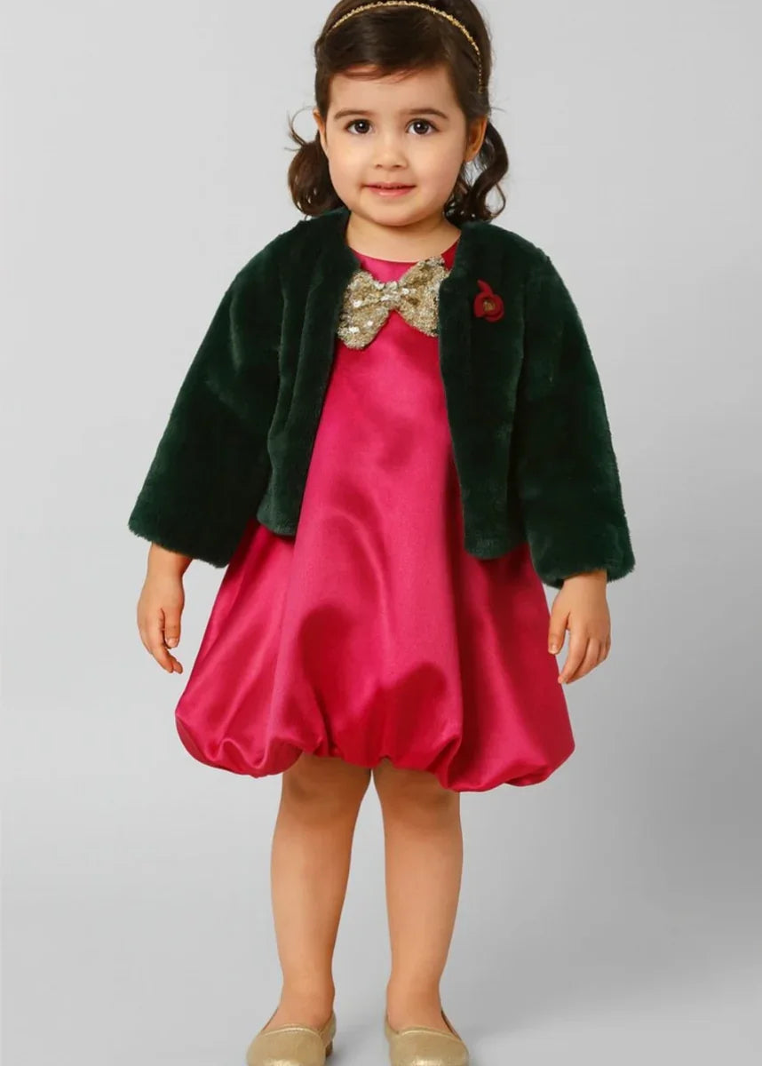Toddler girl in pink satin dress with green faux fur jacket and gold sequin bow
